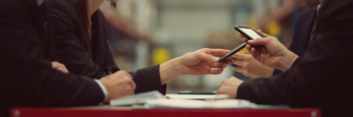 Two colleagues on a warehouse floor reviewing a handheld scanner device.